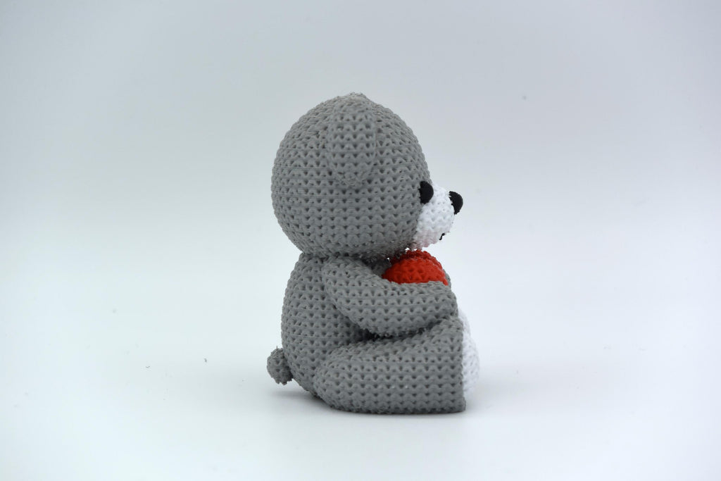 Gray crochet teddy bear holding a red heart on a white background