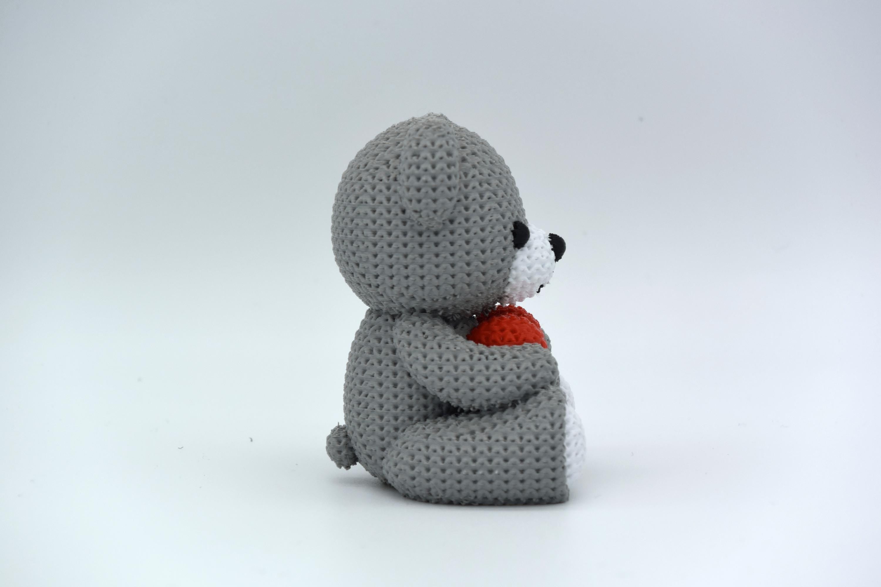 Gray crochet teddy bear holding a red heart on a white background